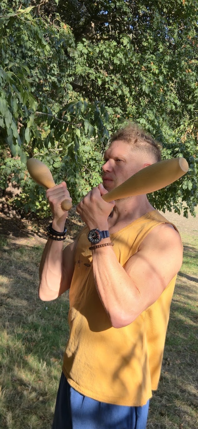 Matt swinging a pair of Indian clubs under a tree